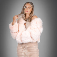 A model wearing a pink, tri-panelled, faux fur coat with a loose fit and wide sleeves, paired with a beige dress and tan sandals.