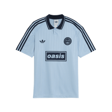 Light blue polo shirt with Adidas and Oasis logos on a green background