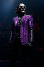 Person wearing a purple suit and black mask in a dark setting
