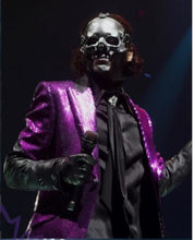 Person wearing a metallic skull mask and purple jacket on a dark background